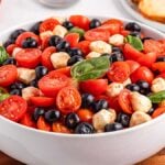 A bowl of blueberry tomato Caprese salad with cherry tomatoes, black olives, mozzarella balls, and fresh basil leaves.