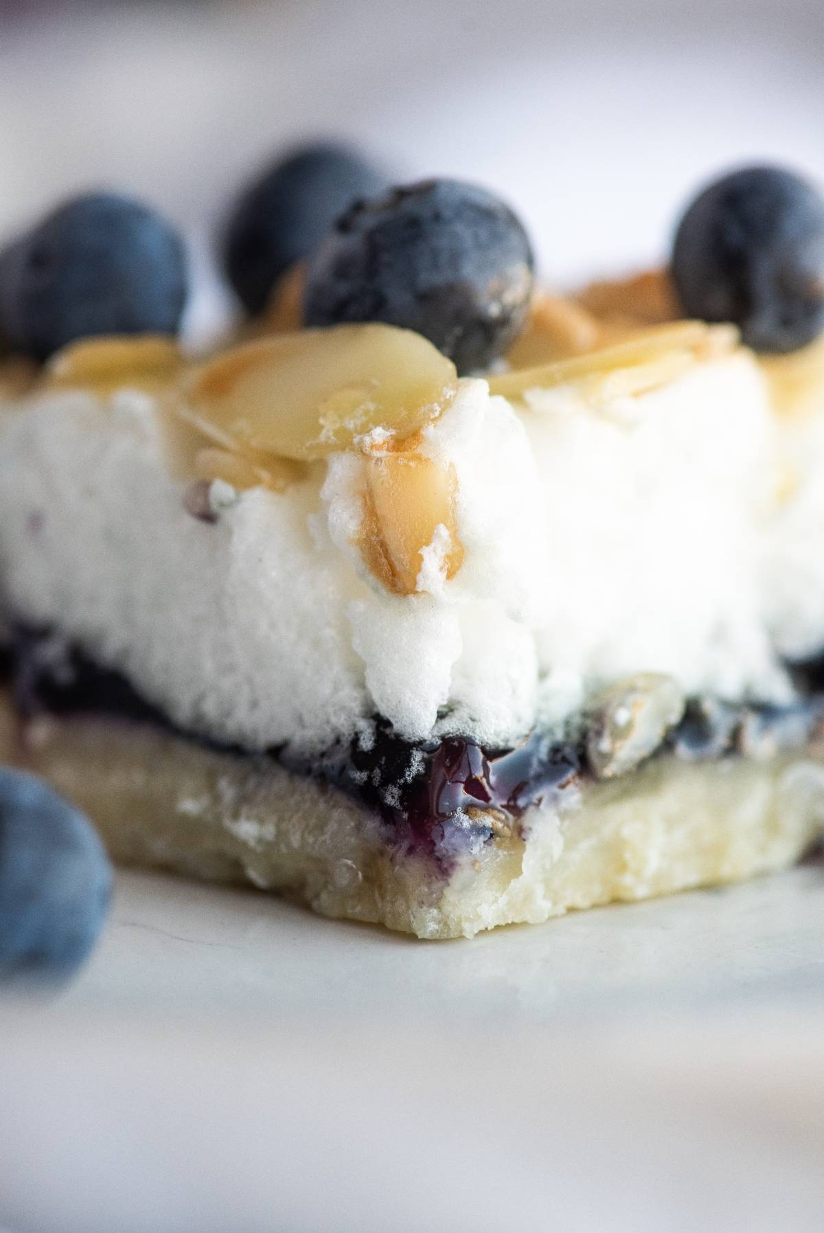 A close-up of almond and blueberry cookie bars topped with blueberries, whipped cream, and almond slices.