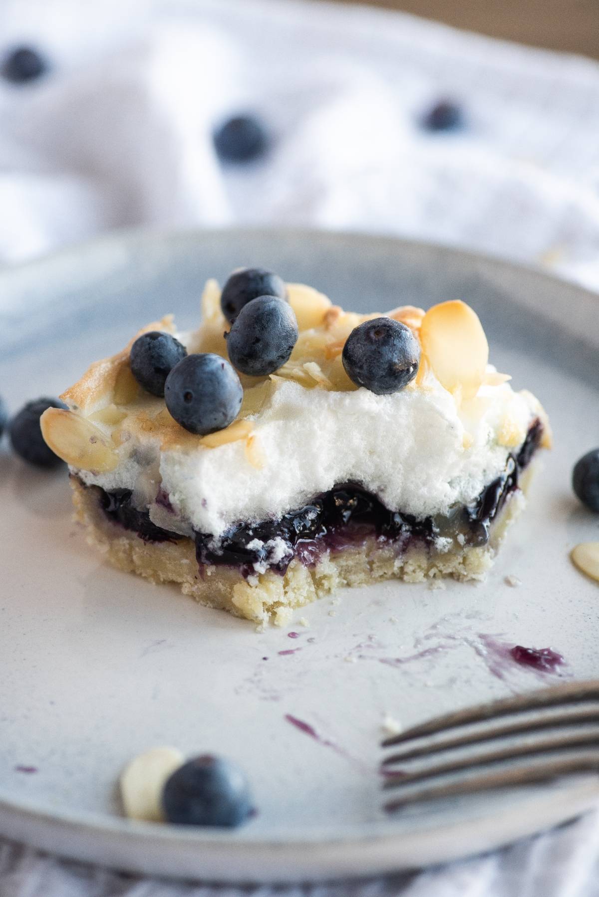 A slice of blueberry dessert bar with a bite taken, topped with whipped cream, blueberries, and almond slices—an easy blueberry dessert recipe perfect for any occasion.