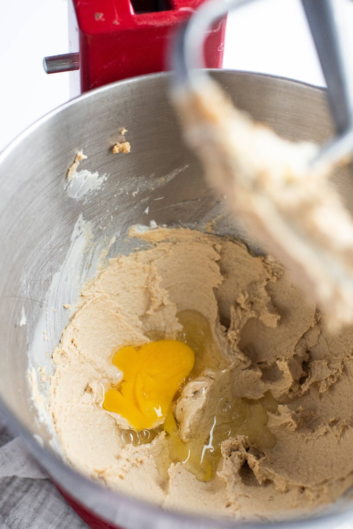 Close-up of a metal mixing bowl with creamed batter and a cracked egg, attached to a red stand mixer—perfect for making almond and blueberry cookie bars or any recipe using blueberry pie filling.