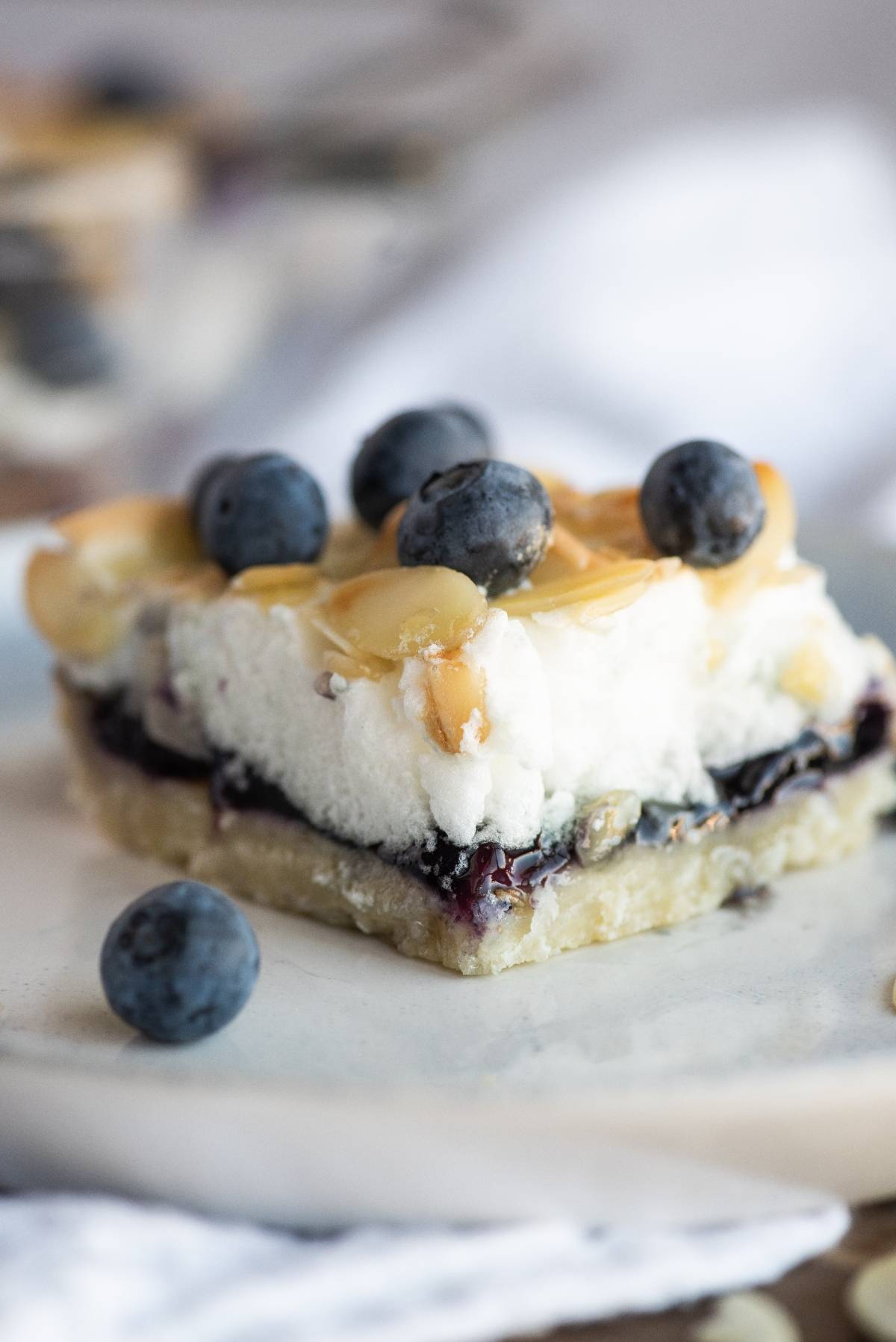 A dessert bar topped with whipped cream, blueberries, and sliced almonds on a light plate—an easy blueberry dessert recipe perfect for any occasion.