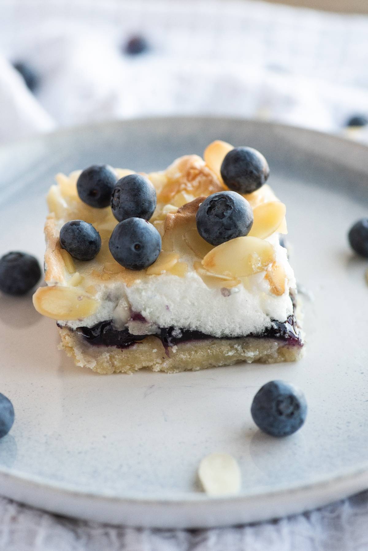 A dessert bar inspired by Blueberry Pie Meringue Squares, topped with whipped cream, blueberries, and sliced almonds on a gray plate.