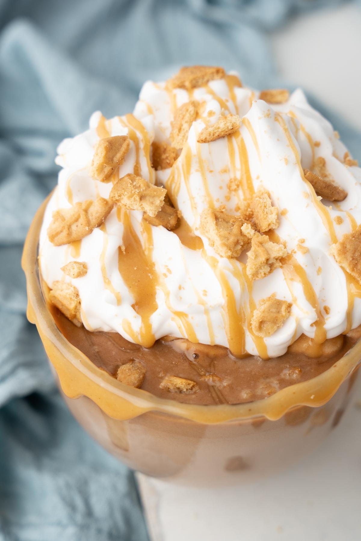A bowl of chocolate ice cream topped with whipped cream, caramel drizzle, crumbled cookies, and a hint of peanut butter hot cocoa for a rich, indulgent twist.