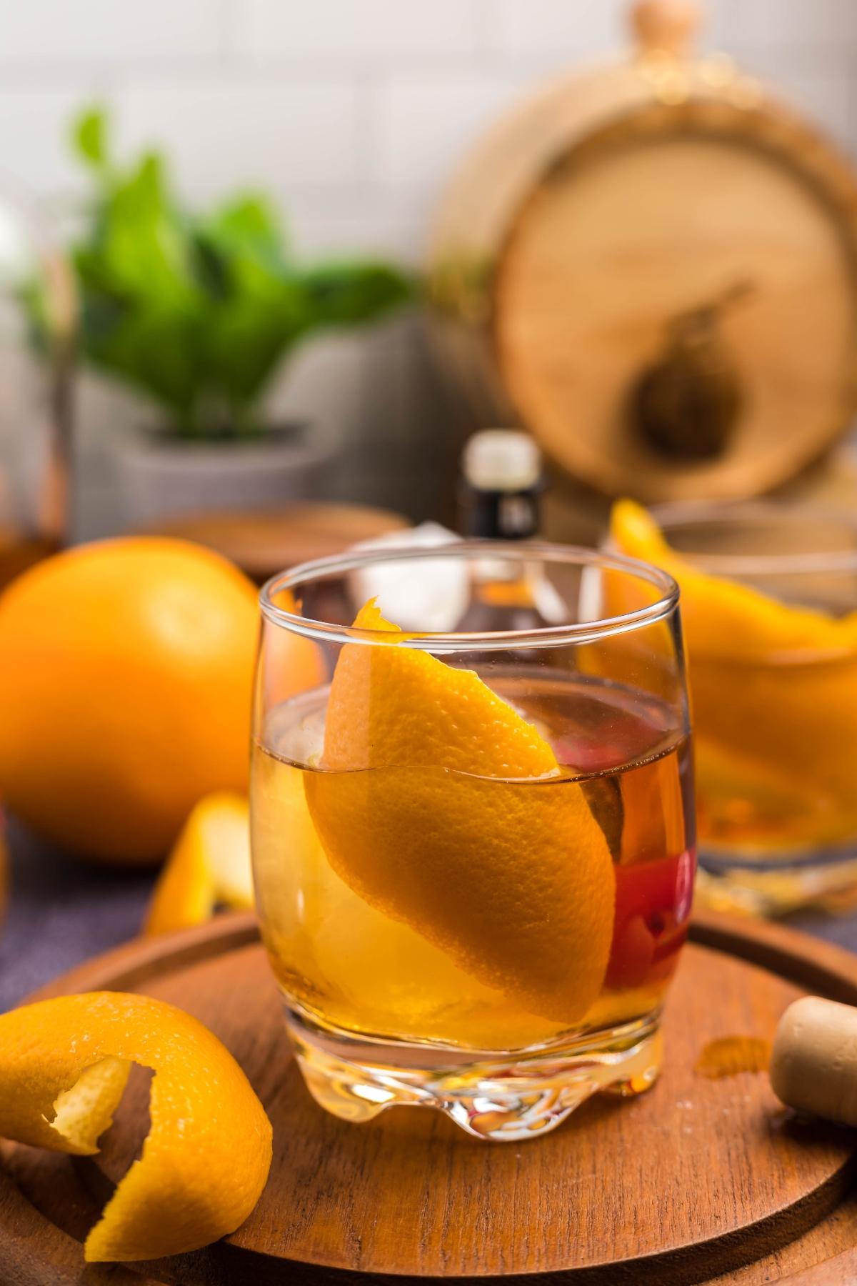 A glass of Bourbon old fashioned cocktail with an orange peel garnish, placed on a wooden tray with oranges nearby—a classic bourbon cocktail perfect for any occasion.