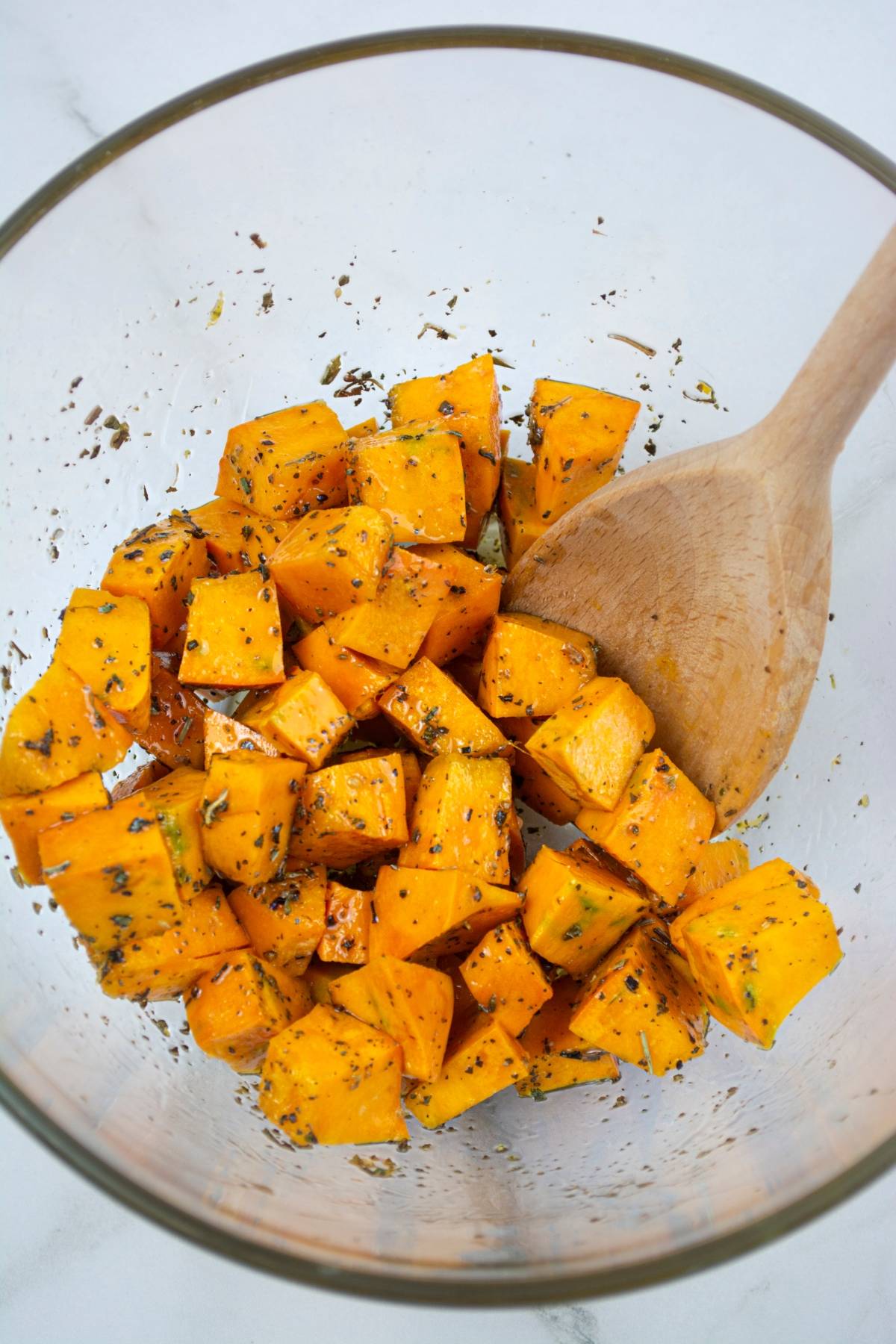 Cubed sweet potatoes with herbs in a glass bowl, stirred with a wooden spoon—a perfect base for a vibrant roasted squash salad.