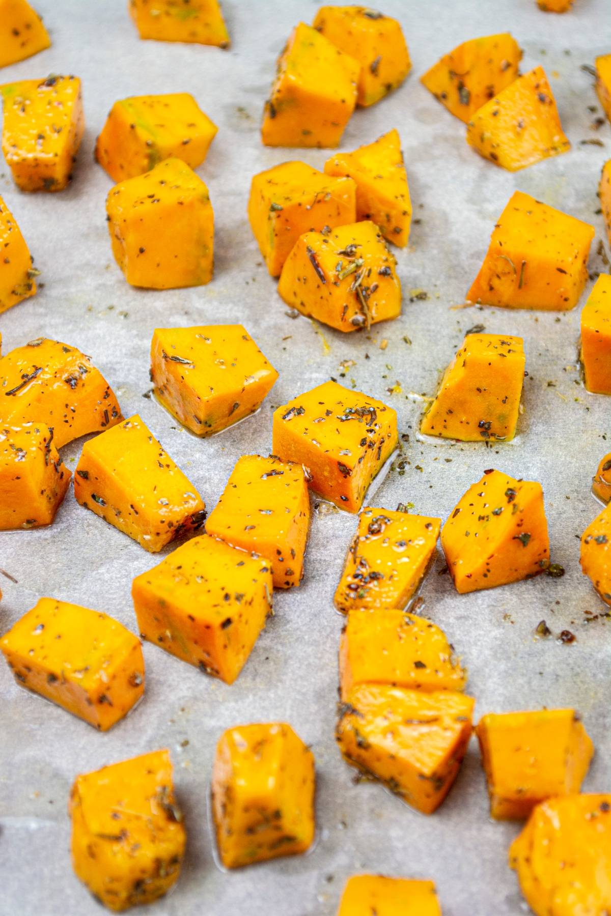 Cubed sweet potatoes seasoned with herbs on a parchment-lined baking sheet, perfect for adding to a roasted squash salad or pairing with your favorite gluten free vegan pasta.