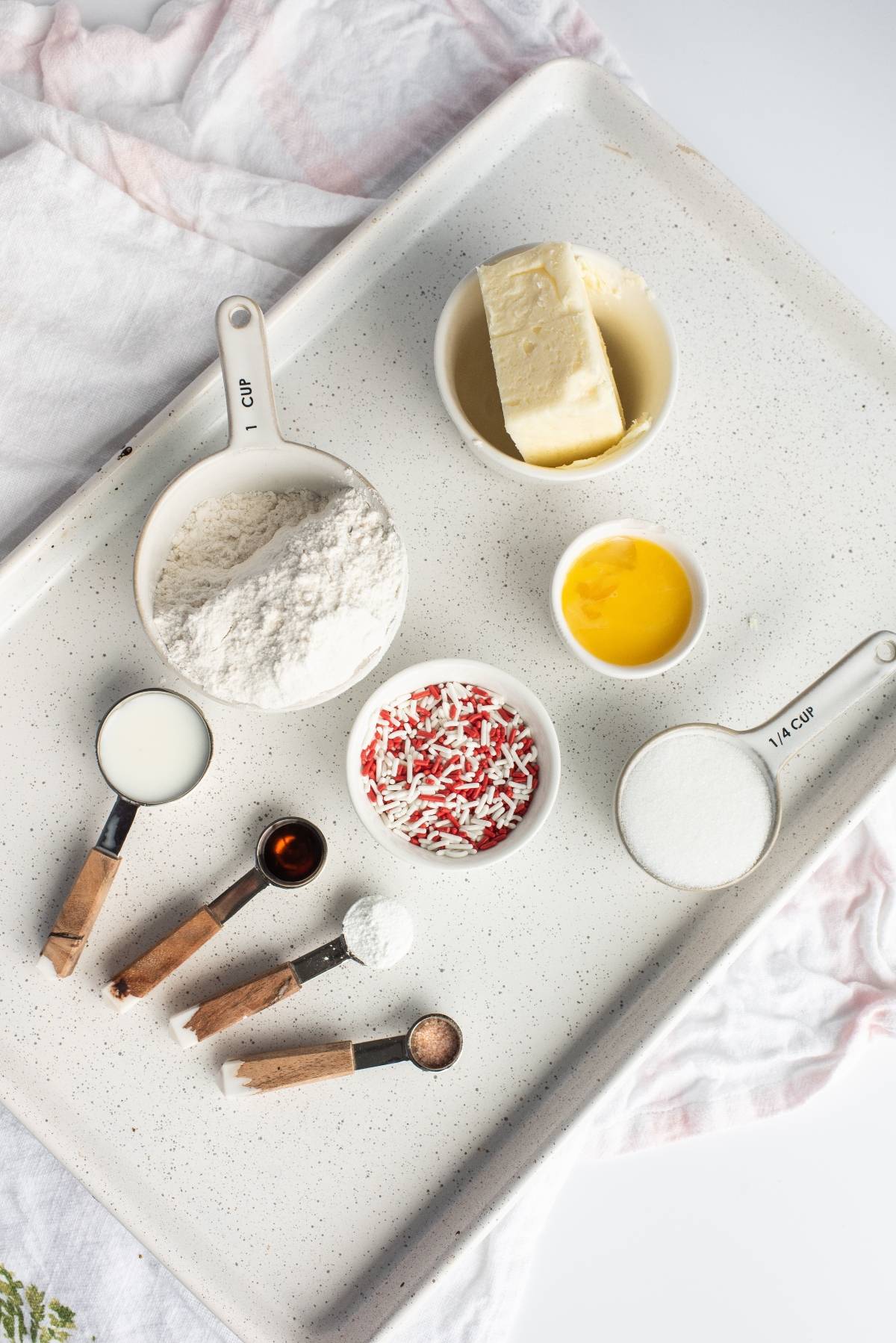 Baking ingredients on a tray: flour, butter, egg yolk, sugar, sprinkles, milk, vanilla, and spices in measuring cups—perfect for recipes for a Canada Day party or red and white Canada Day cookie creations.