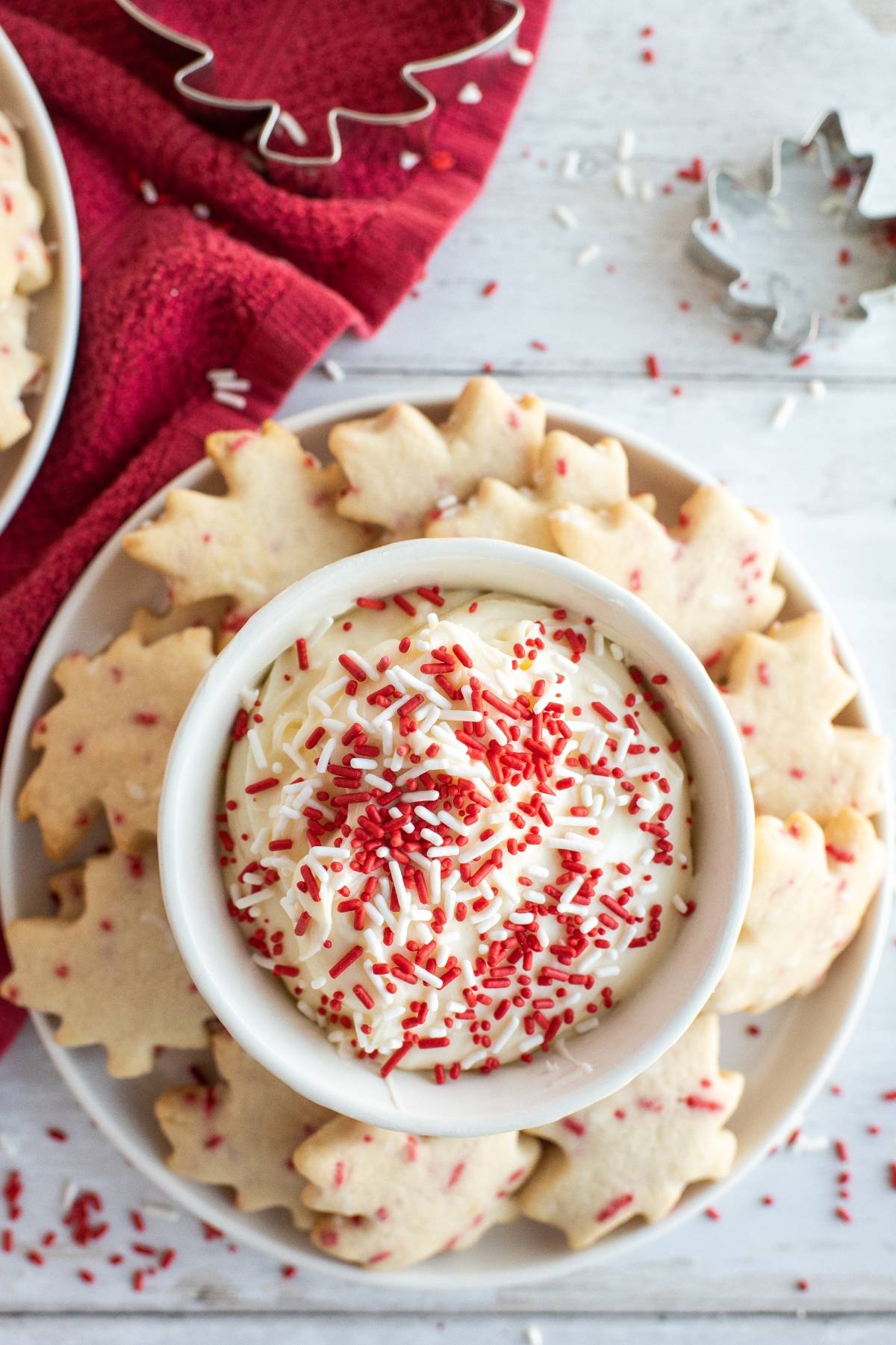Bowl of white dip with red sprinkles, surrounded by maple leaf cookies on a white plate—perfect red and white Canada Day cookie treats to celebrate Canada Day in style.