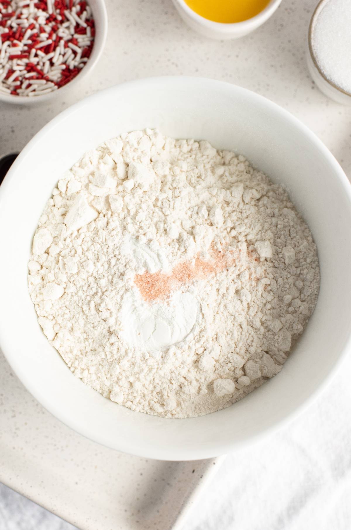 A white bowl filled with flour and baking powder, with bowls of sprinkles and other ingredients nearby—perfect for whipping up Canada Day cookies or trying new Canada Day dessert ideas.