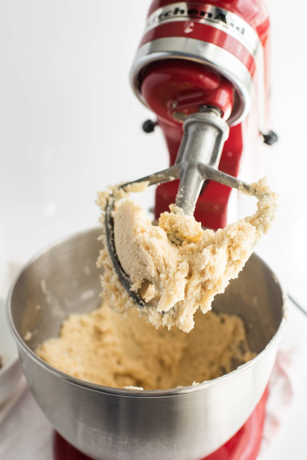 Red stand mixer with paddle attachment mixing cookie dough in a stainless steel bowl—perfect for baking red and white Canada Day cookies to celebrate Canada Day.