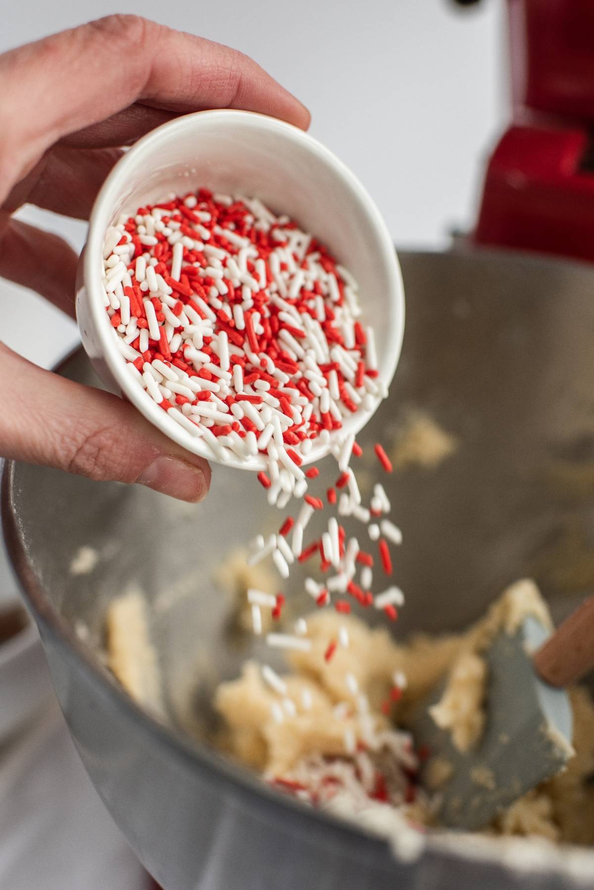 Hand pouring red and white sprinkles from a small bowl into cookie dough, perfect for making festive Canada Day cookies and fun Canada Day dessert ideas.