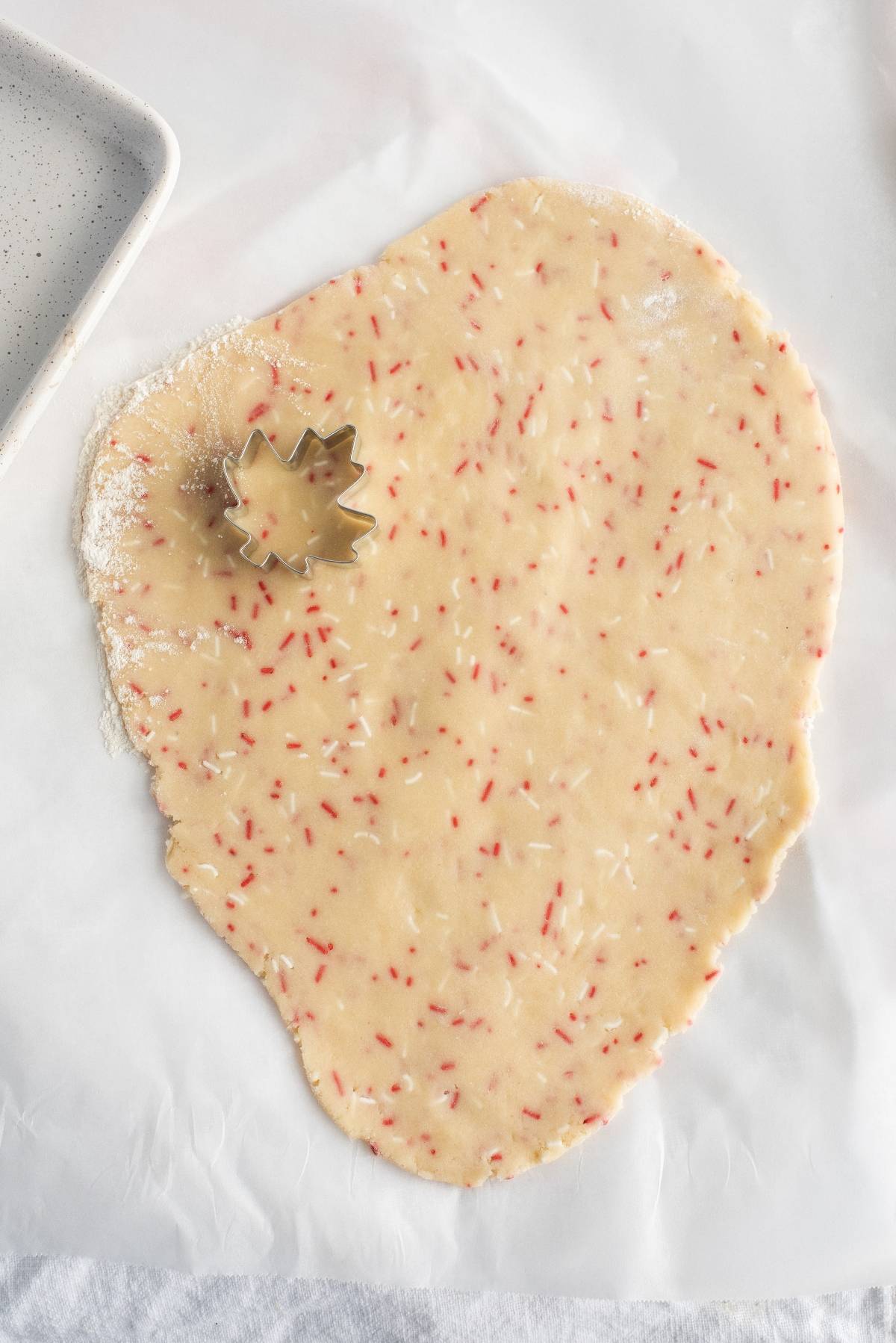 Rolled cookie dough with red sprinkles and a maple leaf cookie cutter on parchment paper—perfect for creating festive red and white Canada Day cookies to celebrate with your favorite recipes for a Canada Day party.