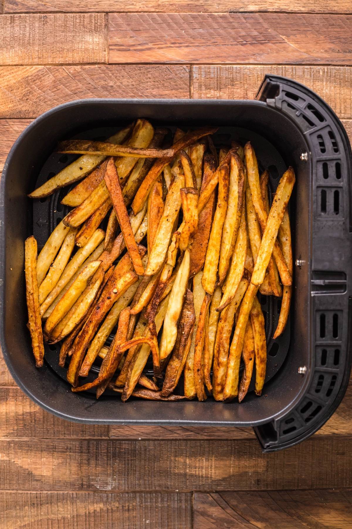 Golden brown French fries in an air fryer basket on a wooden surface, perfect for creating Smothered Fries with Cheese Curds or trying out the best poutine gravy recipe.