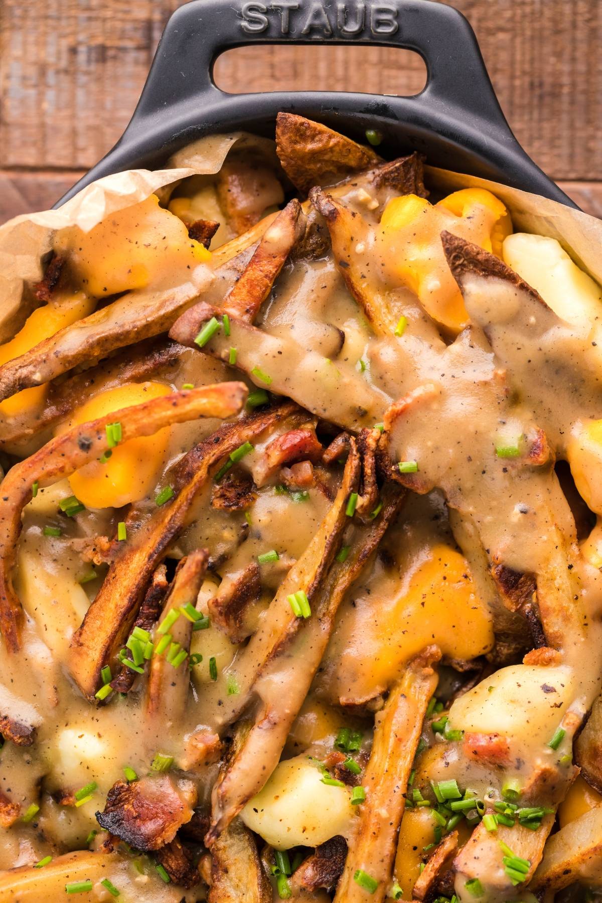 A skillet of Smothered Fries with Cheese Curds, savory gravy, crispy bacon, and chopped chives on top—perfect if you're searching for the best poutine gravy recipe.