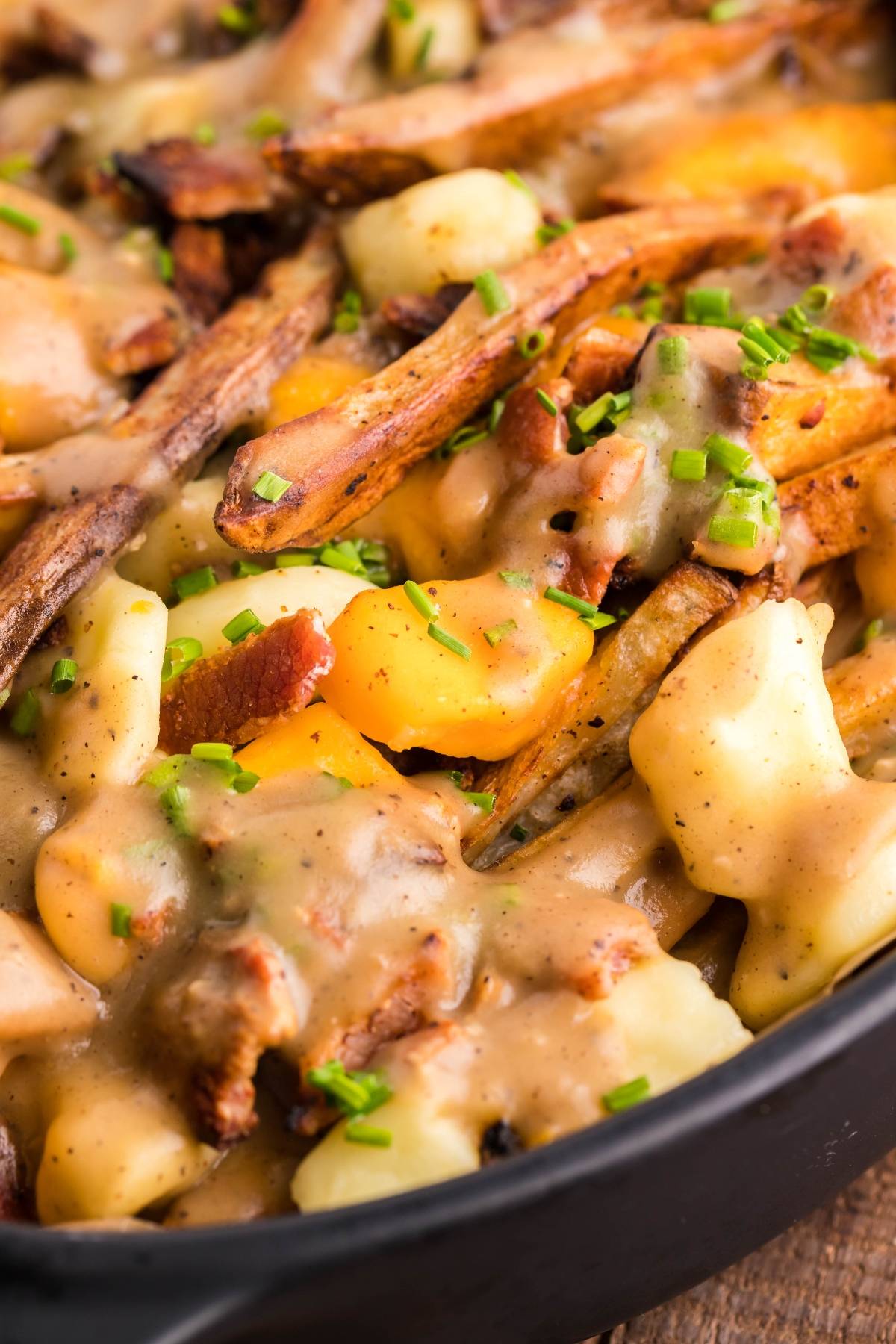 Close-up of Canadian poutine featuring crispy fries, cheese curds, rich gravy, and chopped chives in a black dish—perfect inspiration if you're searching for the best poutine gravy recipe.