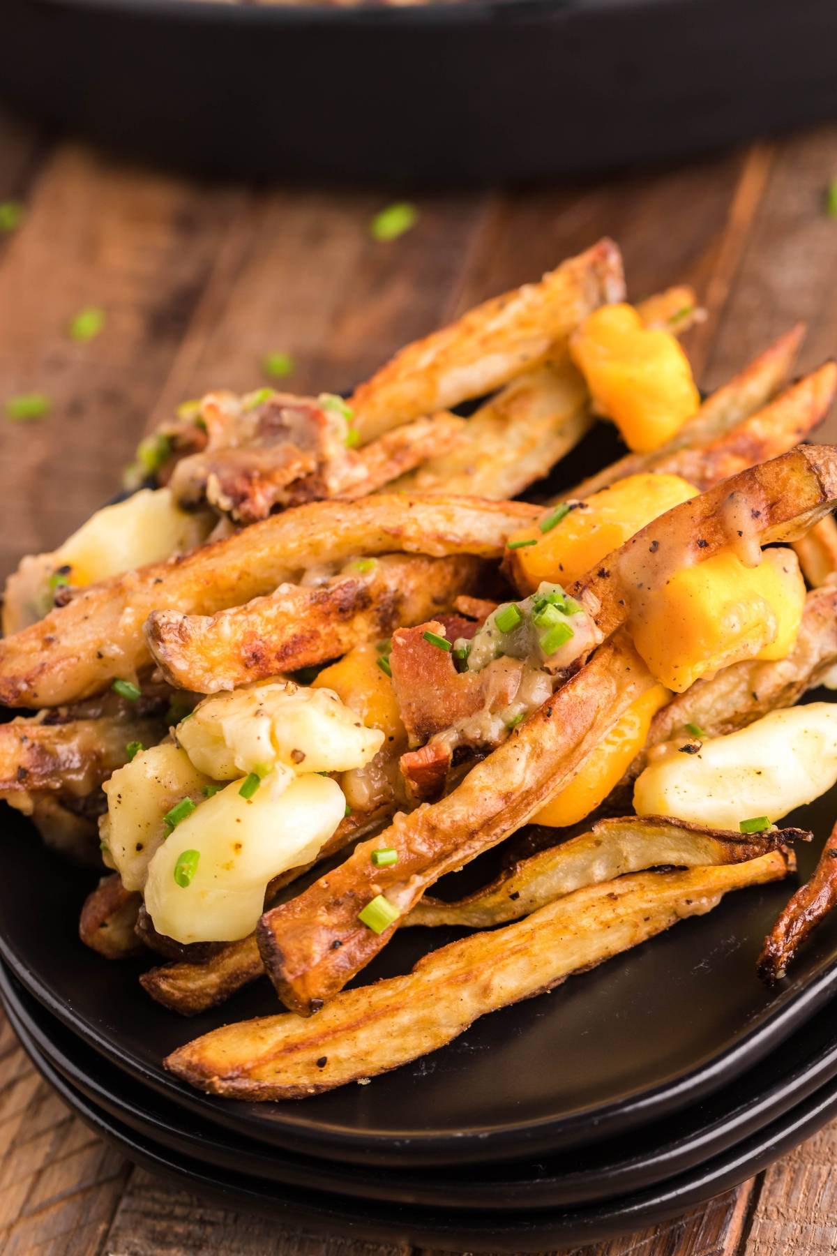 A plate of Smothered Fries with Cheese Curds topped with the best poutine gravy recipe and chopped green onions, served on a black dish—true Canadian poutine at its finest.