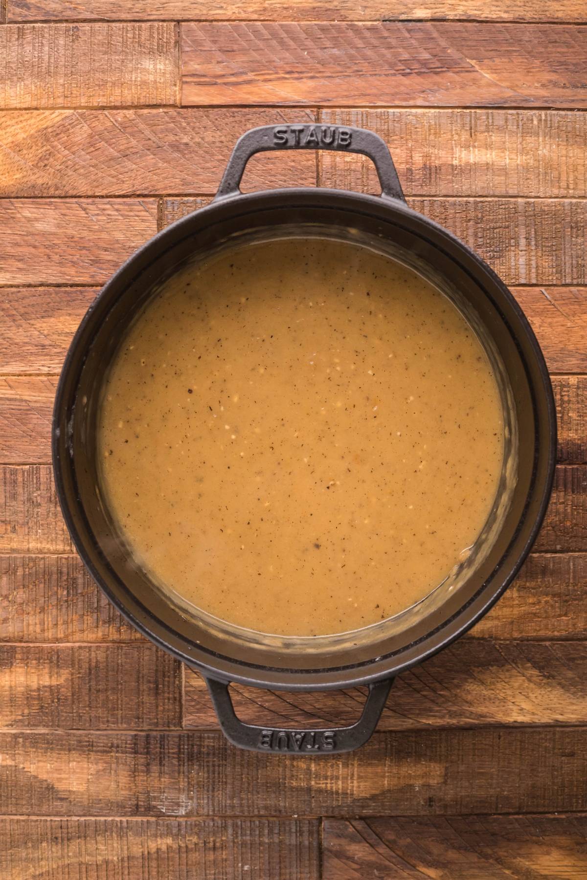 Overhead view of a pot filled with creamy brown gravy on a wooden surface, perfect for making a classic Canadian poutine or smothered fries with cheese curds.