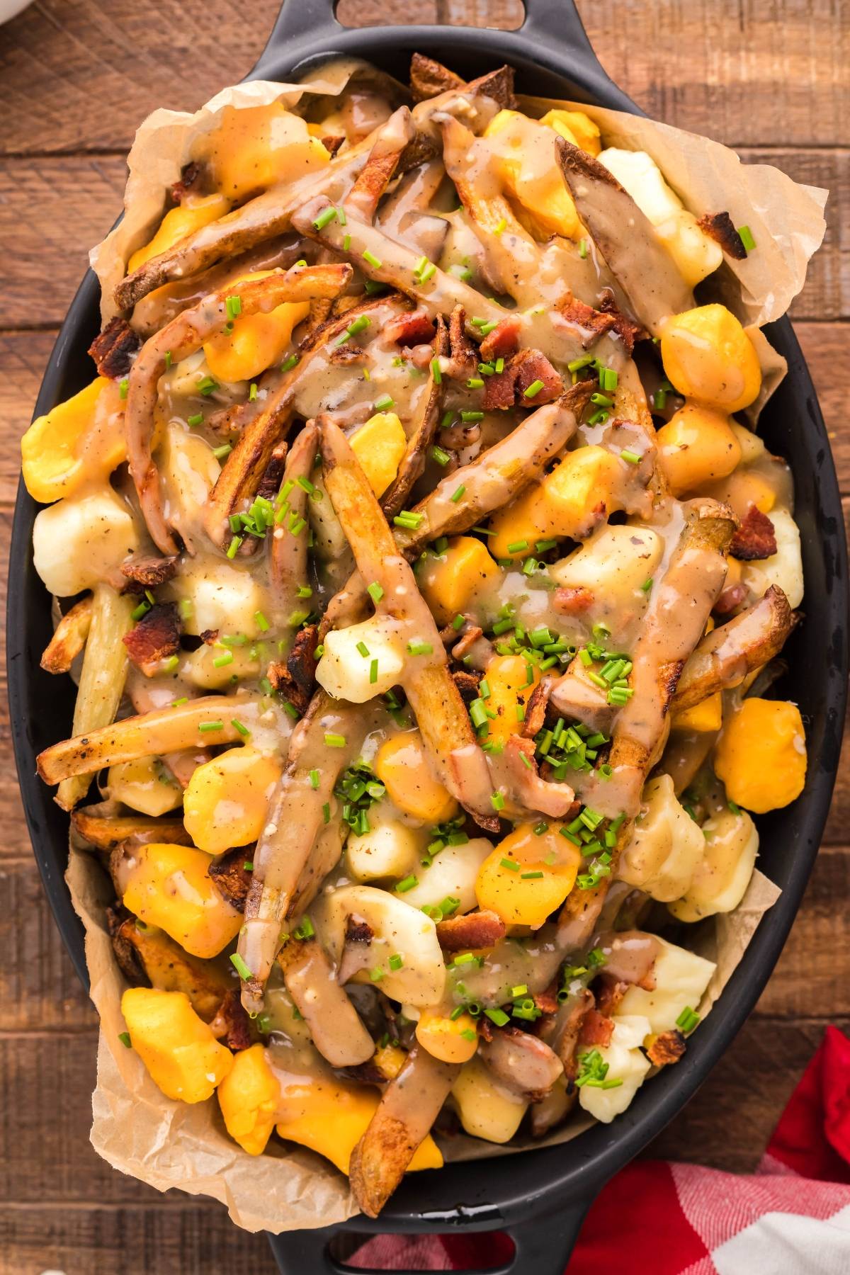 Enjoy authentic Canadian poutine: smothered fries with cheese curds, rich gravy, savory bacon bits, and chopped chives served on a sleek black dish.