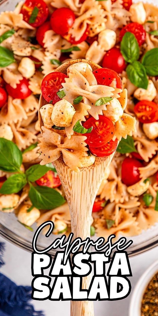 A wooden spoon holds Caprese pasta salad with bowtie pasta, juicy tomatoes, creamy mozzarella, and fresh basil.