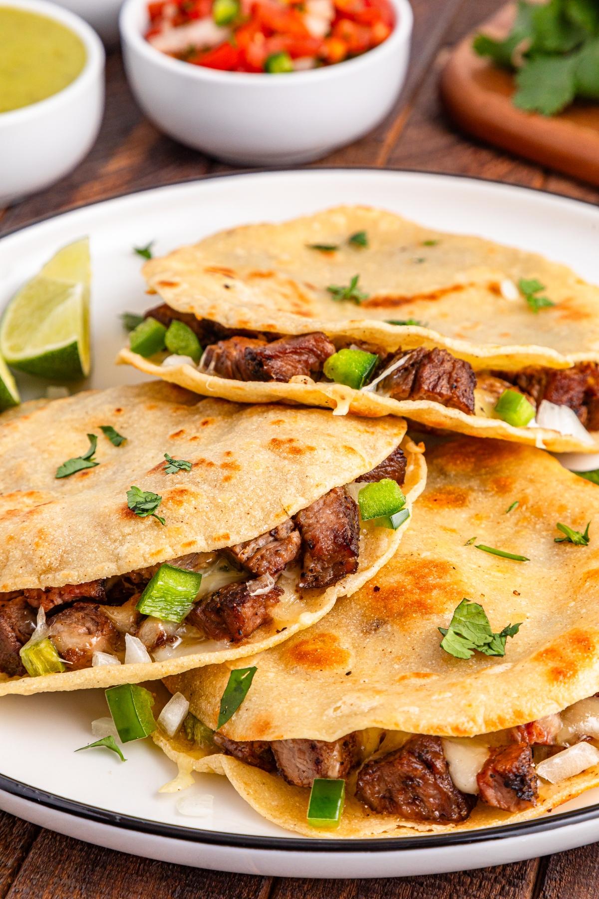 Three beef quesadillas with onions, green peppers, and cilantro on a plate, with lime wedges on the side.