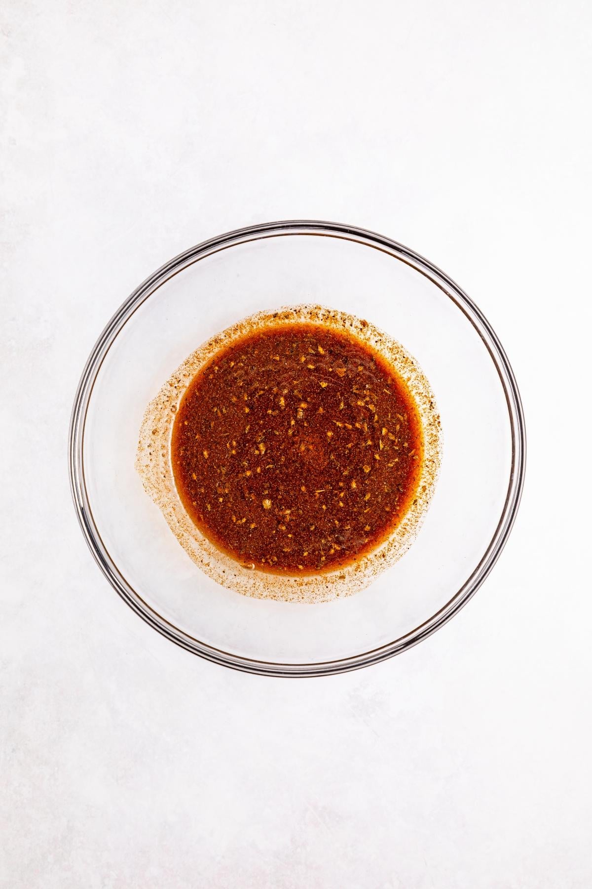 A glass bowl filled with a reddish-brown spice mixture on a white background.