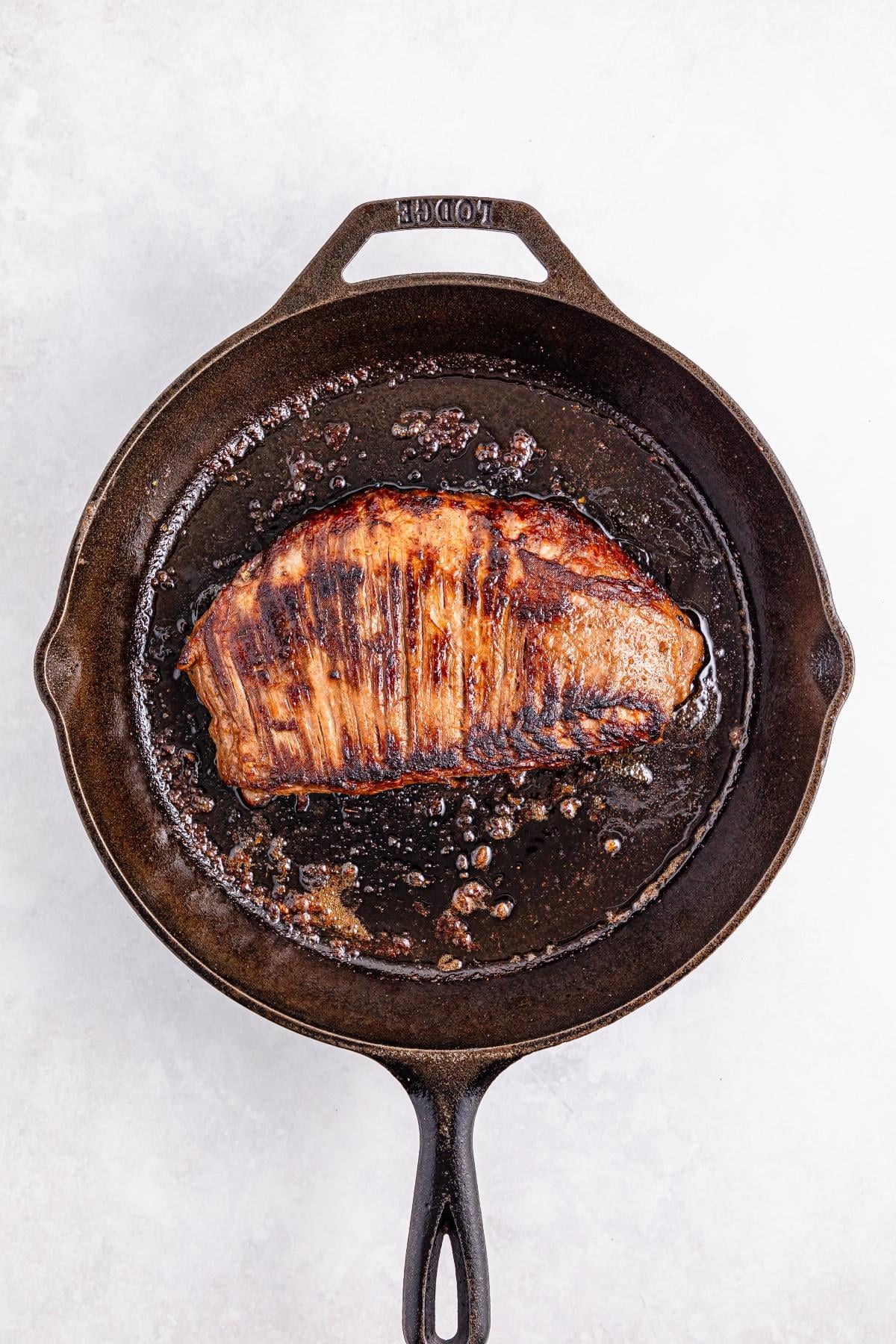 Seared steak cooking in a black cast iron skillet on a white background.