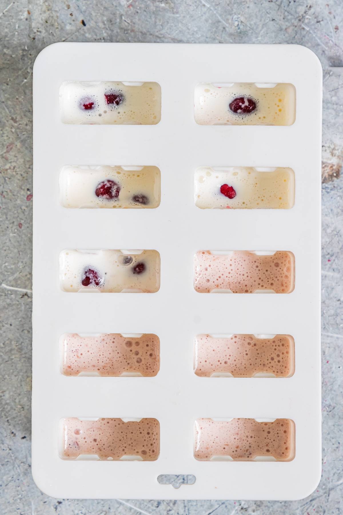 A white ice cube tray holds creamy mixtures with cherries and frothy liquid, creating cherry cheesecake popsicles—the perfect cherry dessert popsicle and a delicious summer treat recipe.
