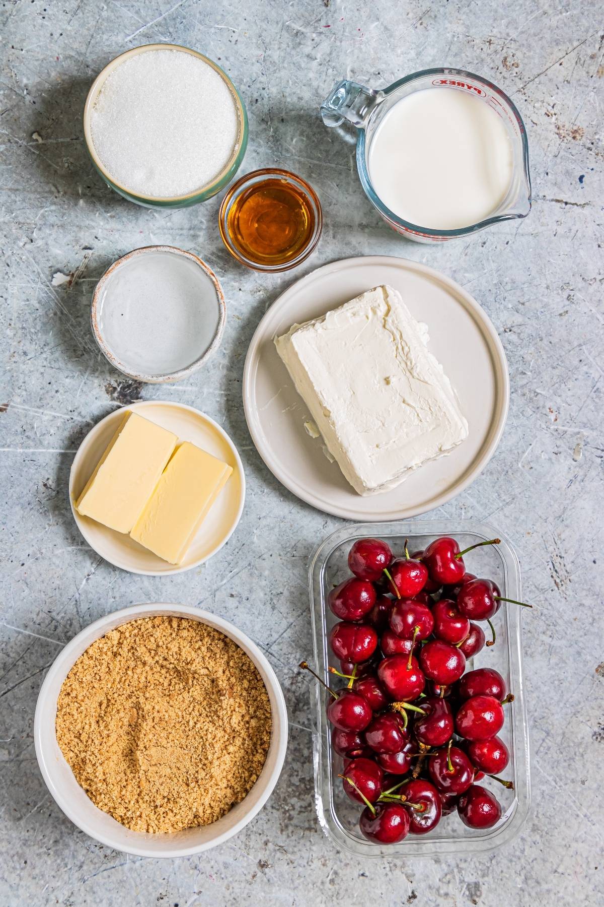 Assorted cheesecake ingredients—cherries, cream cheese, butter, sugar, milk, crumbs, and vanilla—are perfect for a creamy popsicle recipe like Cherry Cheesecake Popsicles, making a delightful summer treat recipe.