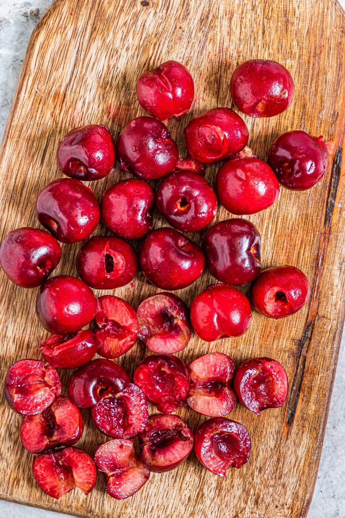 Whole and halved cherries on a wooden cutting board—perfect for your next summer treat recipe or as a vibrant topping for Cherry Cheesecake Popsicles.