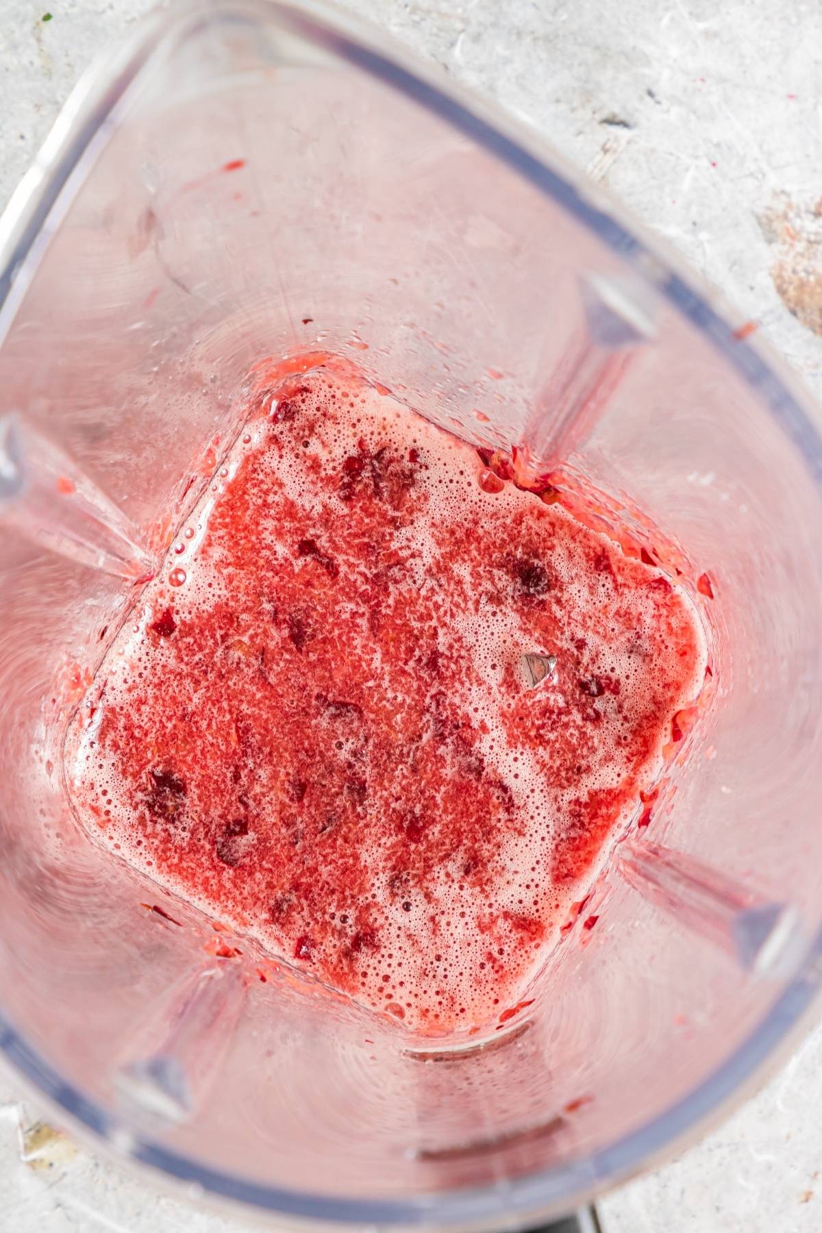 Close-up of a blender with partially blended red fruit mixture and foam inside, perfect for a refreshing summer treat recipe.