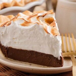 A decadent slice of chocolate meringue pie rests on a plate with a gold fork, while the remaining chocolate meringue pie sits elegantly in the background.