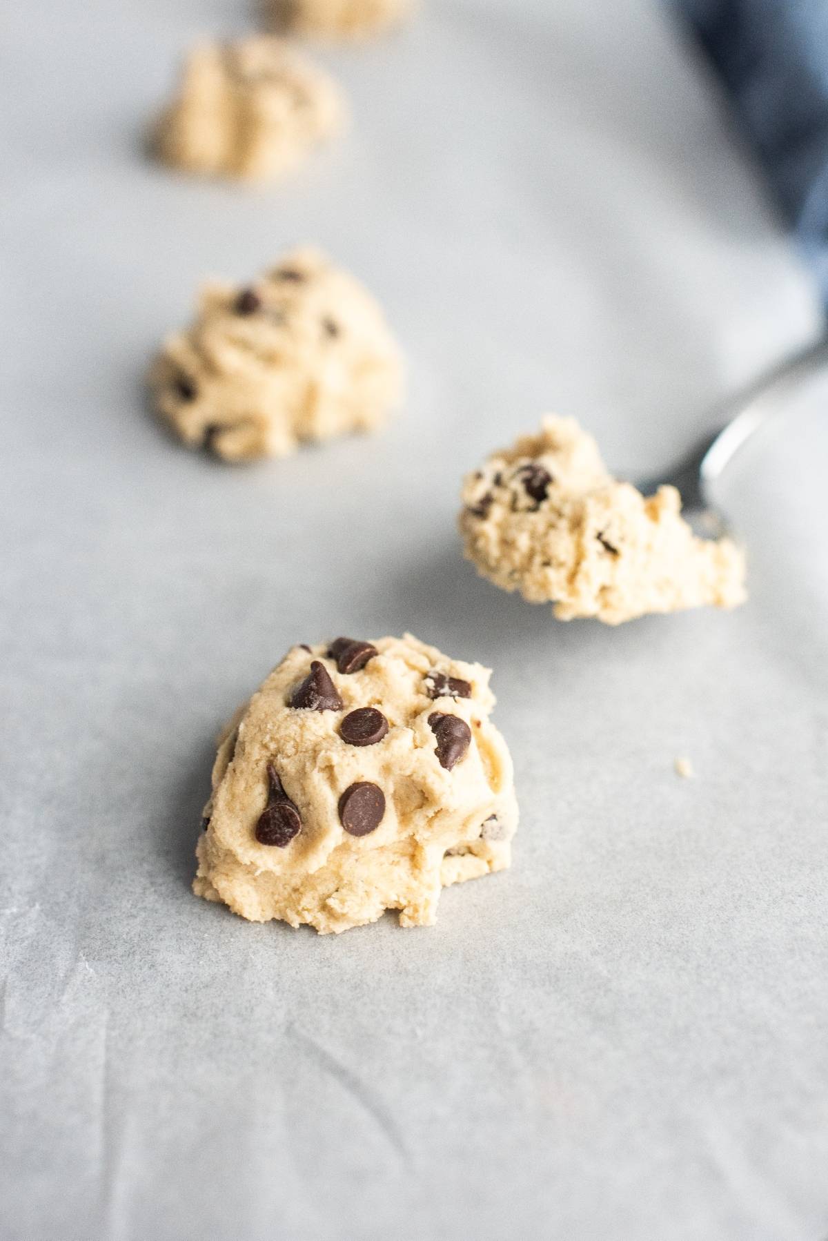 Spoon scooping chocolate chip cookie dough onto a parchment-lined baking sheet, perfect for making Chocolate Chip Buttercream Sandwiches—the best filling for sandwich cookies.