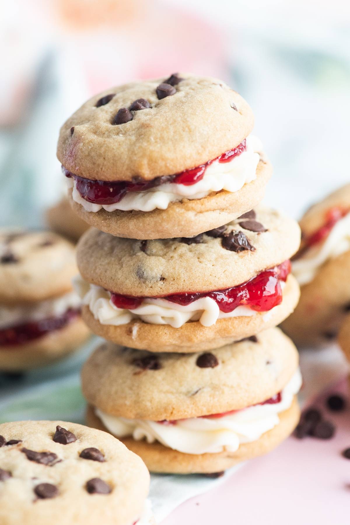 Stacked Chocolate Chip Buttercream Sandwiches filled with white cream and red jam, with more cookies in the background, showcase the best filling for sandwich cookies.