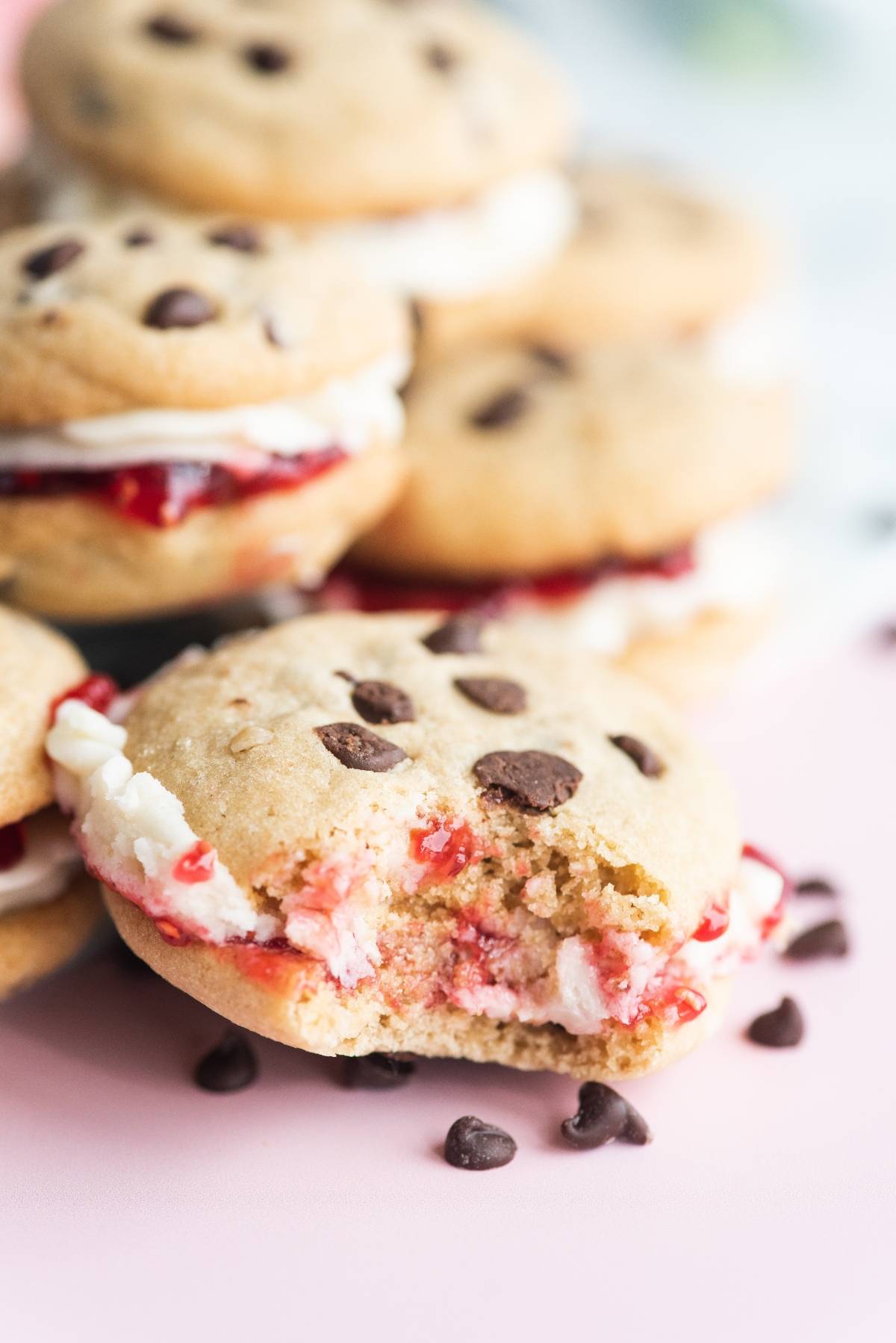 A bitten chocolate chip cookie sandwich with cream and jam filling, surrounded by more cookie sandwiches—showcasing the best filling for sandwich cookies.