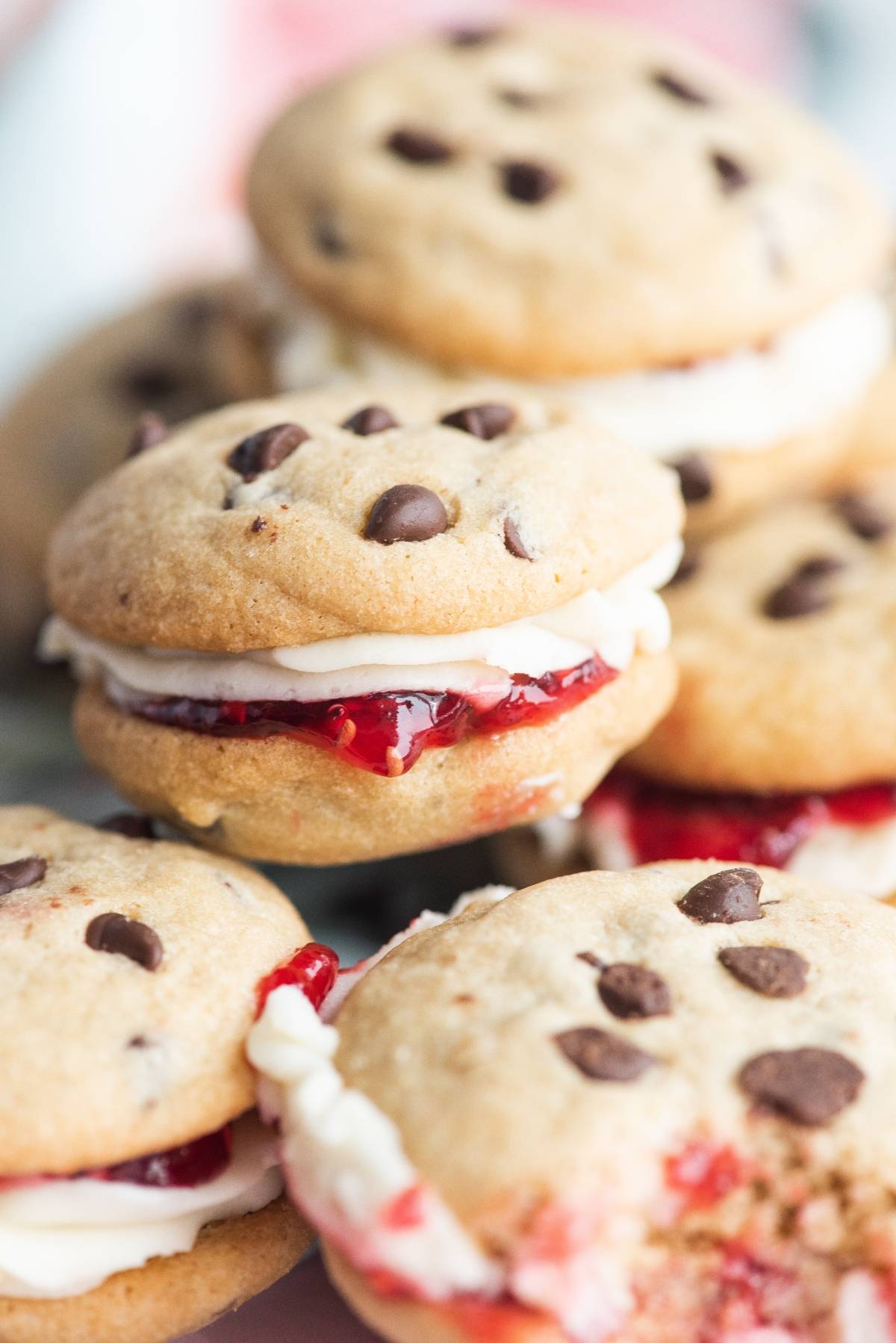 Chocolate chip cookie sandwiches filled with cream and strawberry jam, stacked closely together—these are the best sandwich cookies with jam for lovers of decadent sandwich cookie filling.