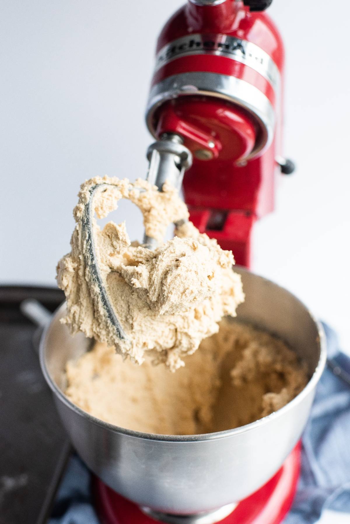 A red stand mixer with cookie dough on the paddle attachment and in the metal mixing bowl—perfect for whipping up sandwich cookie filling or making Chocolate Chip Buttercream Sandwiches.