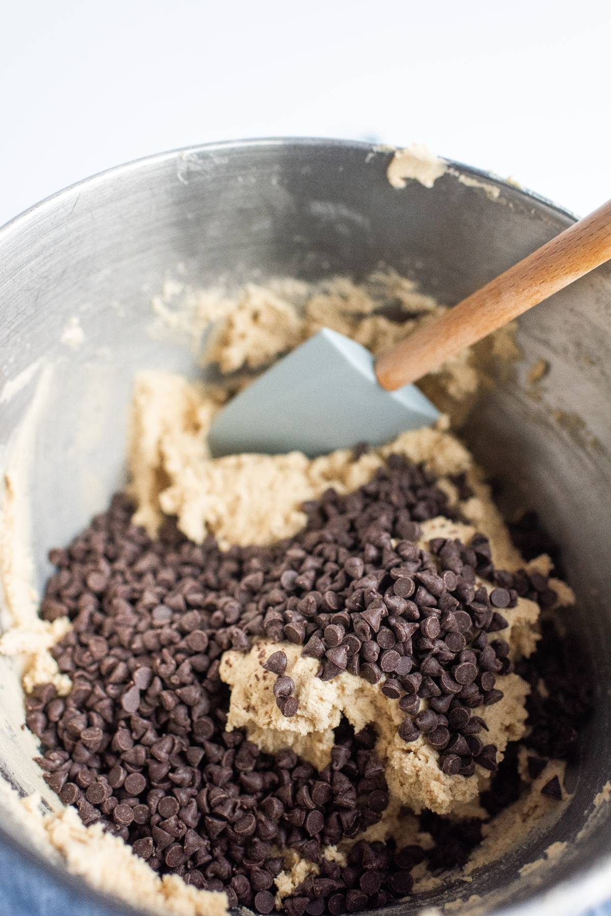 Chocolate chips being mixed into cookie dough with a spatula in a metal bowl, perfect for creating the best sandwich cookies with jam or your favorite sandwich cookie filling.