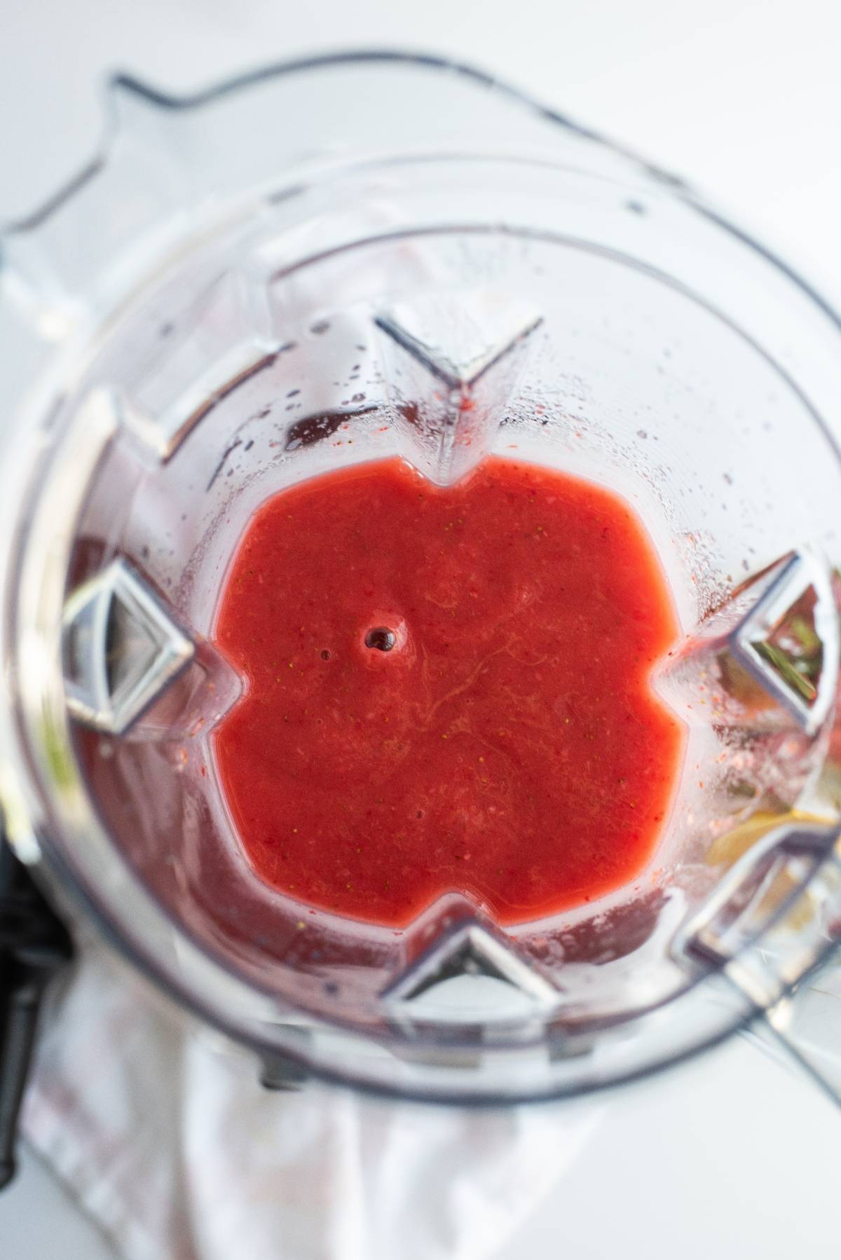 Top view of a blender filled with a bright red, freshly blended liquid, possibly the base for a delicious summer treat recipe or dipped fruit popsicle recipe.
