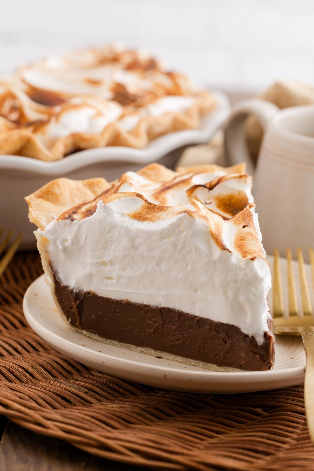 A slice of chocolate cream pie topped with toasted meringue on a plate, with a whole pie in the background.