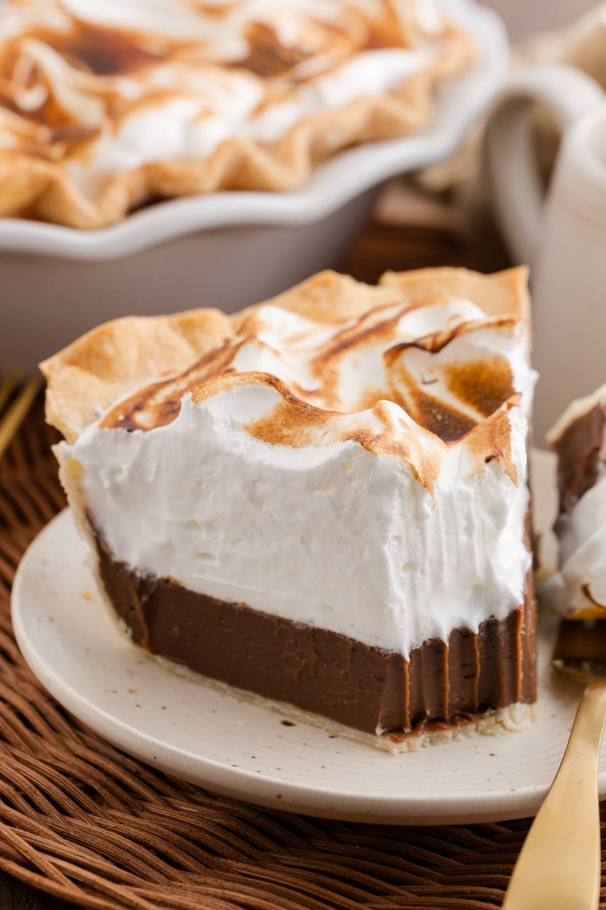Slice of chocolate meringue pie with a golden-brown top on a white plate.