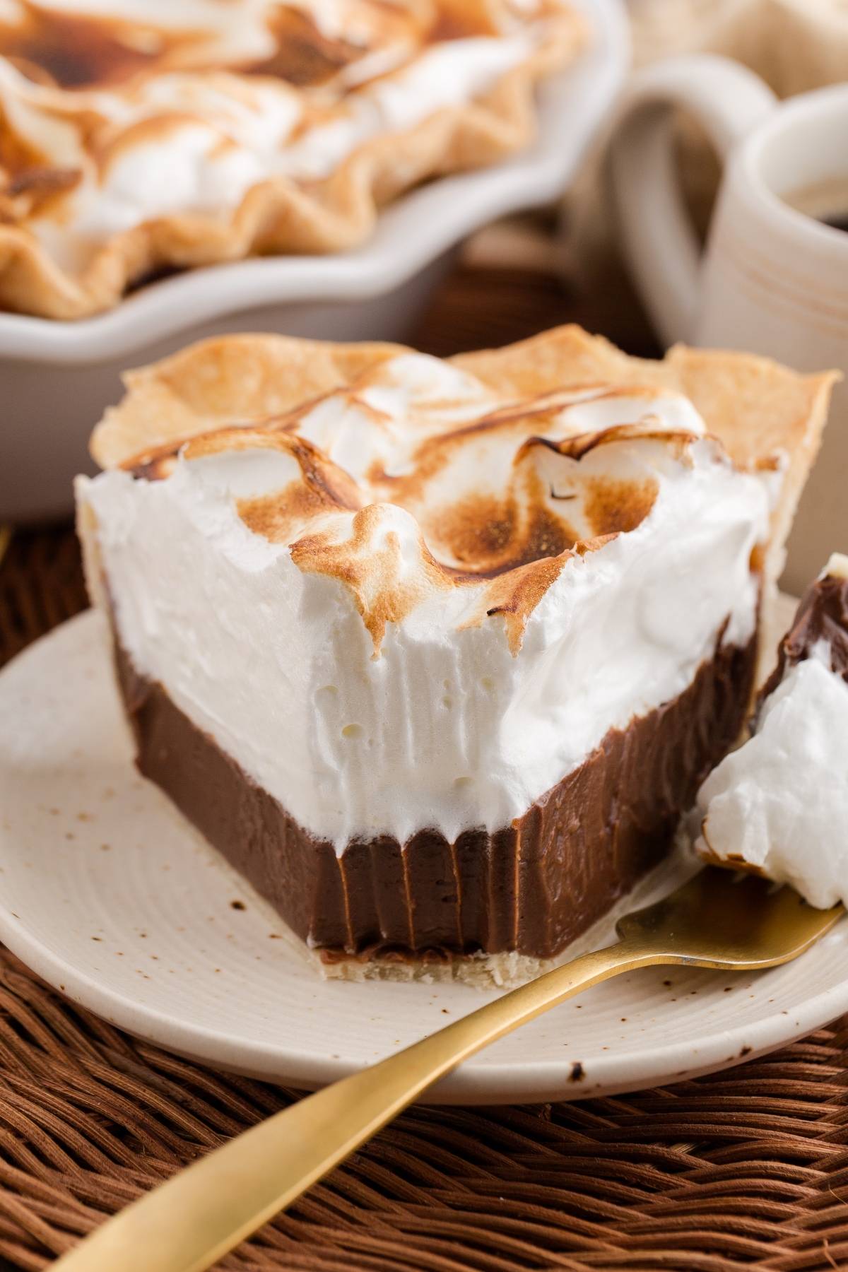 A slice of chocolate meringue pie with a bite taken out, on a plate with a gold spoon.
