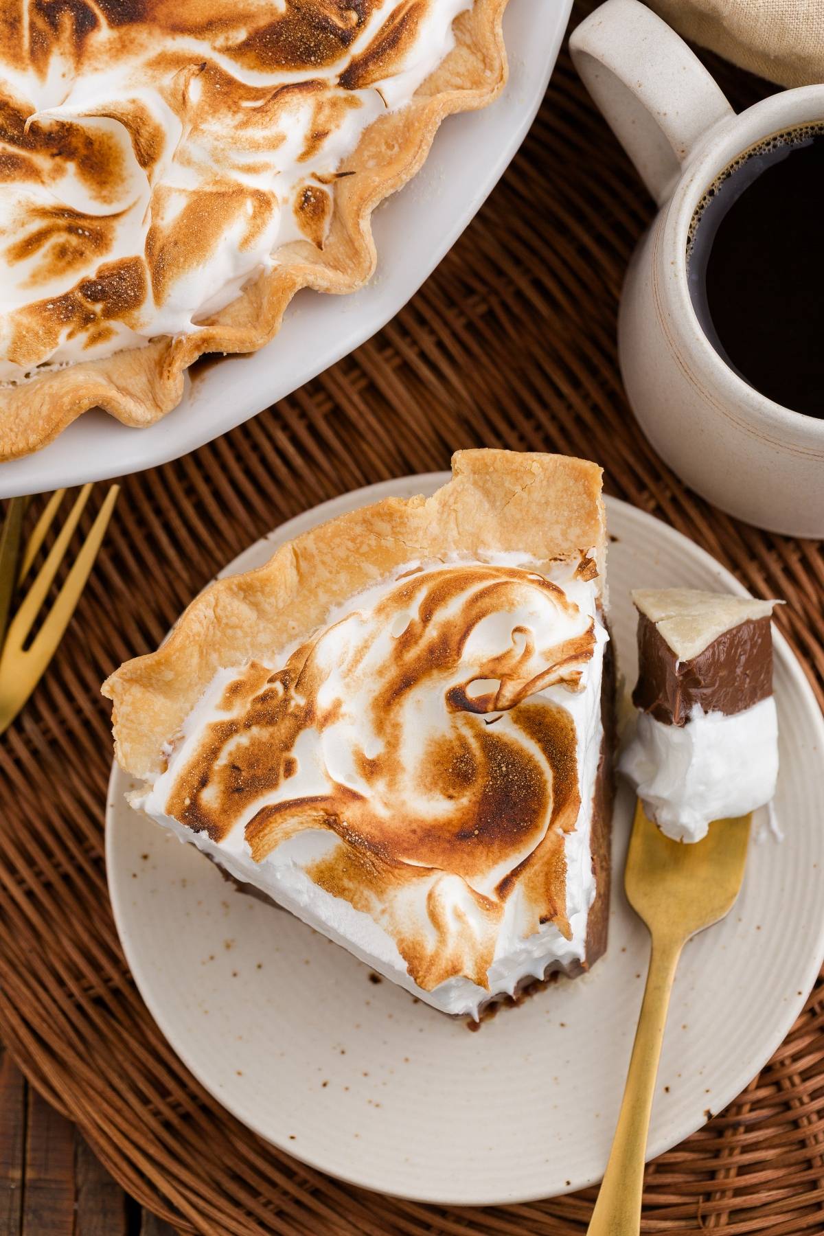 A slice of chocolate meringue pie on a plate with a fork, next to a cup of black coffee.