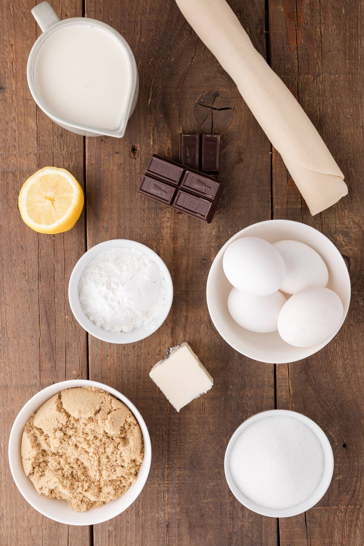 Baking ingredients: eggs, lemon, chocolate, brown and white sugar, butter, powdered sugar, cream, pastry dough.