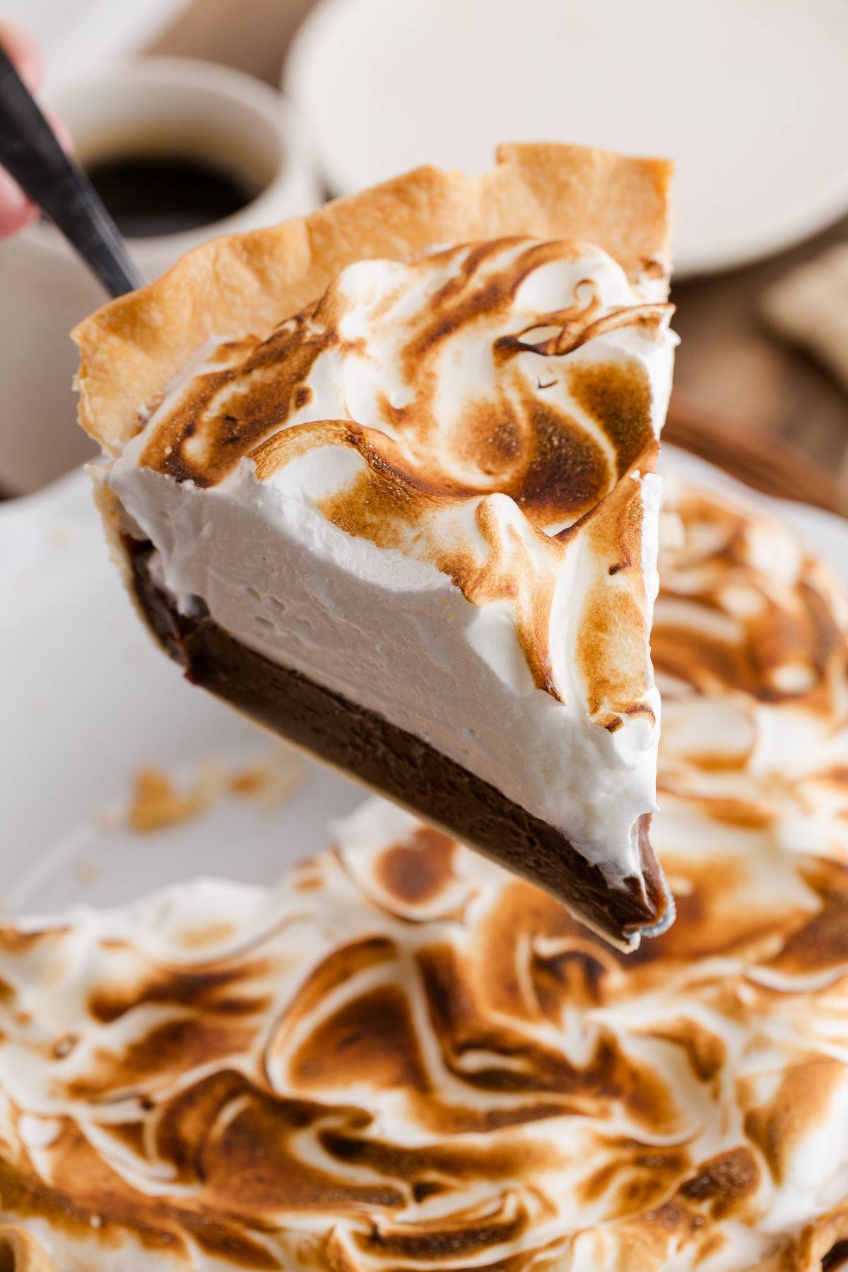 A slice of chocolate meringue pie is being lifted from the whole pie, showing its creamy layers.