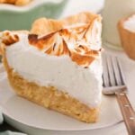 A slice of coconut meringue pie with toasted meringue topping sits on a plate beside a fork.