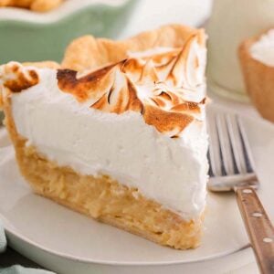 A slice of coconut meringue pie with toasted meringue topping sits on a plate beside a fork.