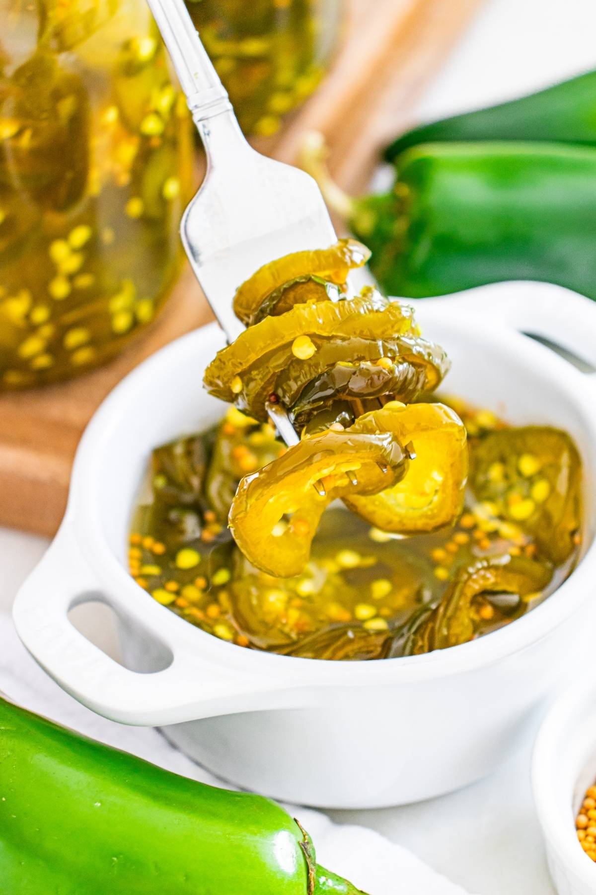 A fork holds sliced pickled jalapeños above a small white bowl filled with more pickled jalapeños.