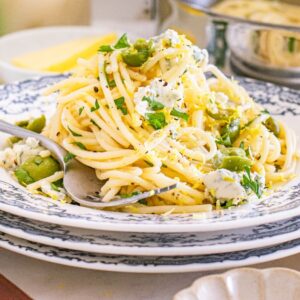 A plate of dirty martini pasta with green olives, cheese, lemon zest, and herbs served on a floral-patterned dish.