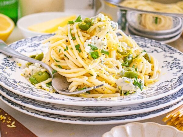 A plate of dirty martini pasta with green olives, cheese, lemon zest, and herbs served on a floral-patterned dish.
