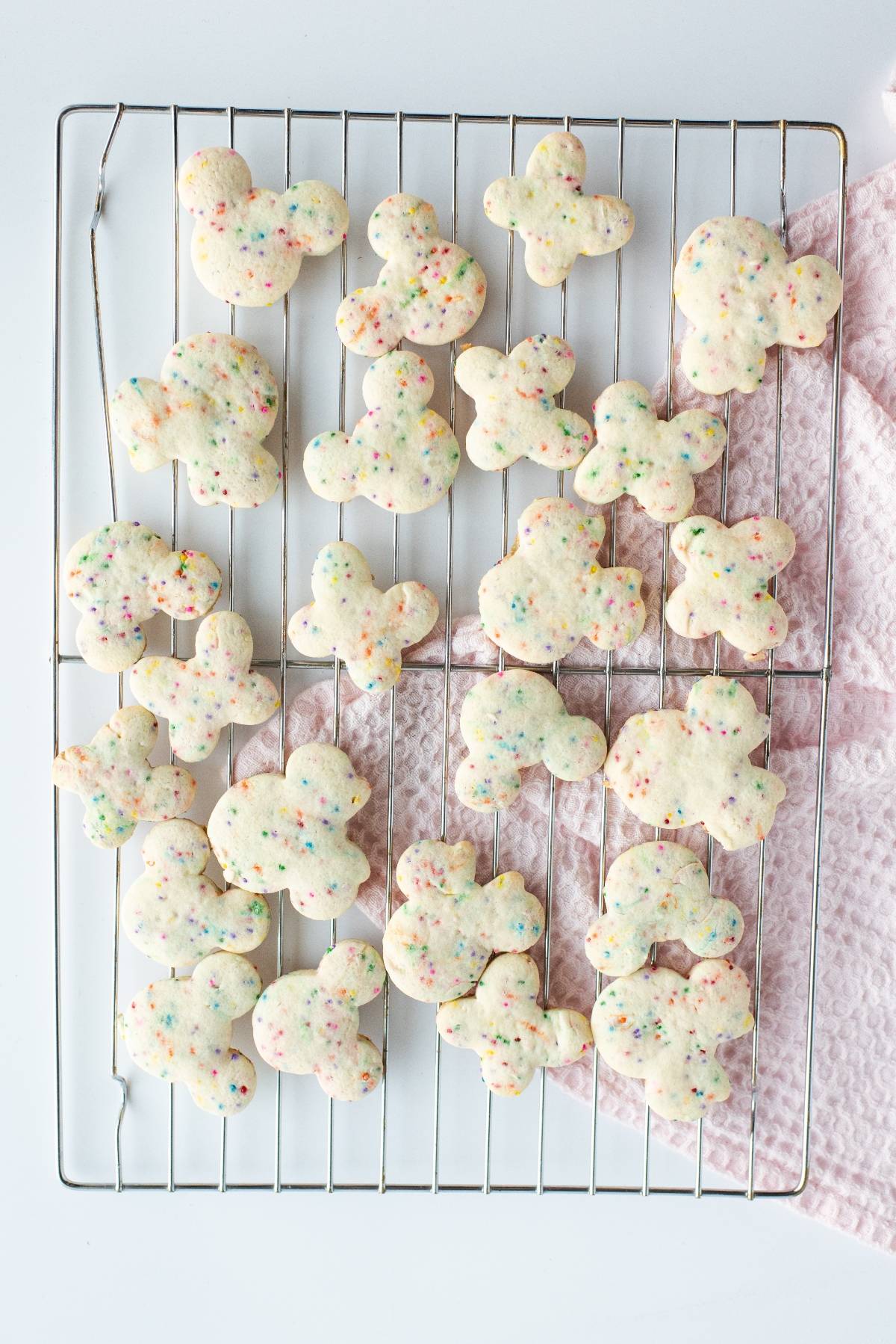 Funfetti cookies in bunny and flower shapes cool on a wire rack over a pink towel, perfect for pairing with Funfetti Dunkaroo dip.